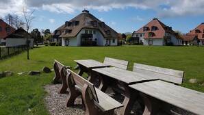 A park with picnic tables and a large building with a thatched roof. - MeerZeit, Germany (Prerow)