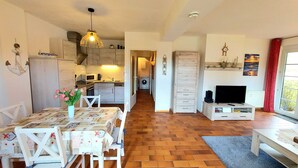 A cozy living room with a TV, a dining table with chairs, a kitchen in the background, and a hallway leading to a laundry area. - MeerZeit, Germany (Prerow)