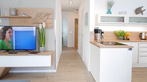 A modern kitchen with white cabinets, a wooden countertop, and a built-in island. There is a television on a stand with a potted plant beside it. - Baabe Villen Ensemble FeWo 15 Strandsonne Ref. 213134 (Baabe)