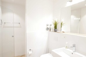 Et moderne badeværelse med en brusekabine i glas, en hvid vask og et spejl over vasken.