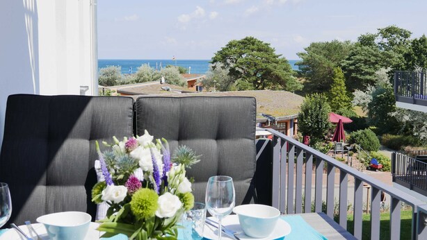 A balcony with a table set for two, overlooking a scenic view of the sea and a coastal area. - Baabe Villen Ensemble FeWo 15 Strandsonne Ref. 213134 (Baabe)