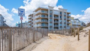 A beachfront apartment building with balconies, a sandy path, and a 'Leave Only Your Footprints' sign. - Sand Pointe - Oceanfront Escape on 41st Street (Ocean City)