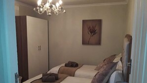 A hotel room with two beds, a chandelier, a painting, and a wardrobe. - Dellville Country House (Kareeberg)