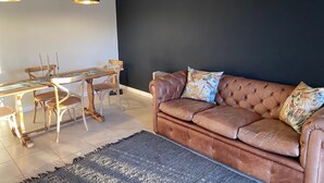 A living room with a brown leather sofa, a dining table with chairs, and pendant lights. - Dellville Country House (Kareeberg)