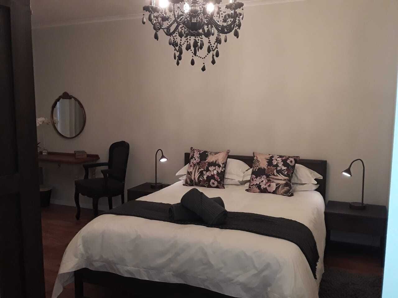 Un dormitorio con una cama grande, dos mesitas de noche, una silla, un espejo y una araña.