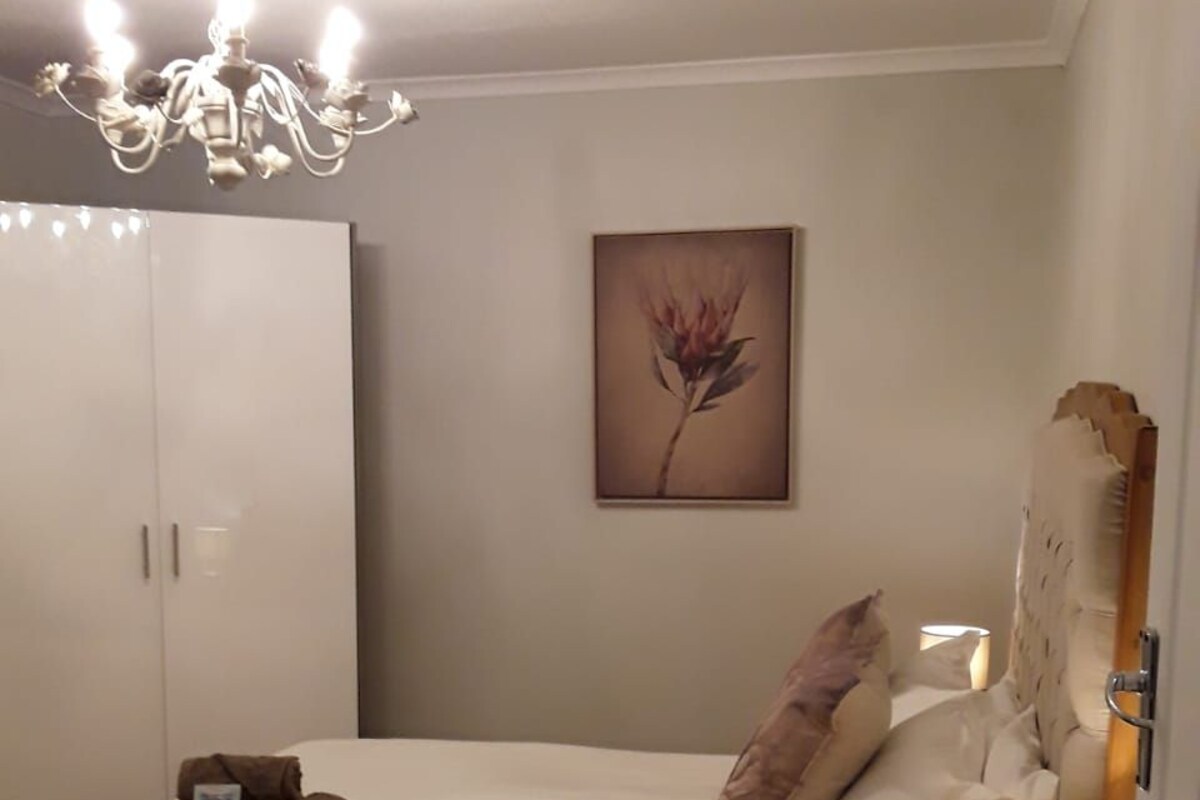 A bedroom with a bed, a nightstand, a lamp, a painting, and a wardrobe.