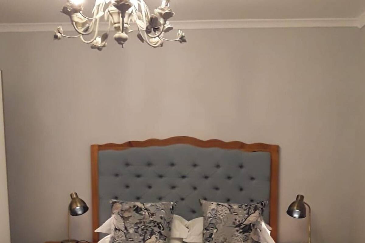 A neatly made bed with a tufted headboard, two bedside lamps, and a chandelier.