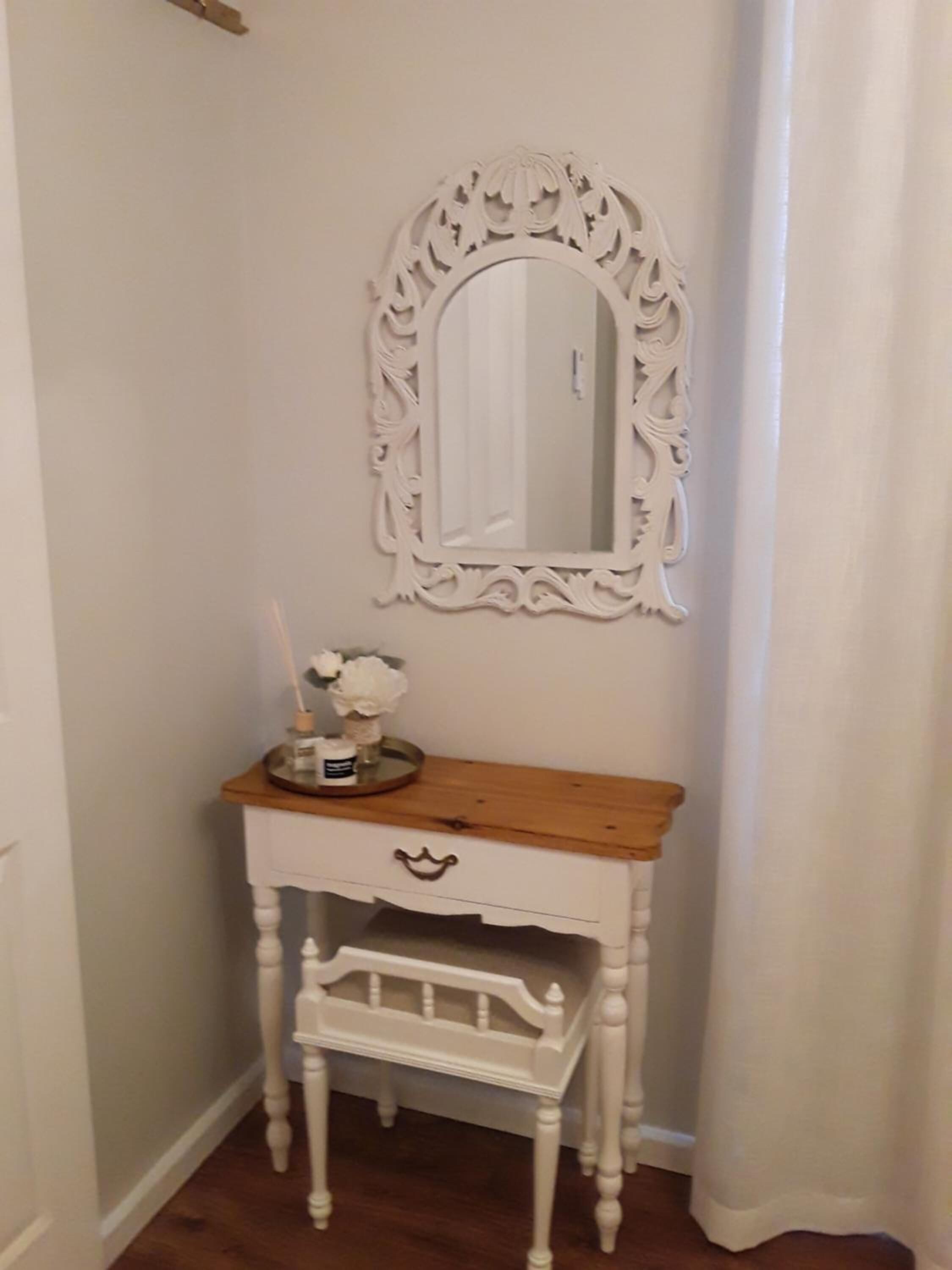 A white vanity with a mirror, a small wooden table, and a drawer.