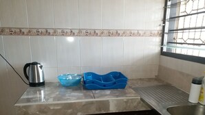 Eine Küche mit einer gefliesten Spritzschutzwand, einem Edelstahlkocher, einer blauen Plastikschüssel und einem blauen Plastikbehälter.