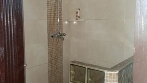 Eine Dusche mit Glasabtrennung, einer gefliesten Wand und einem Ablagefach für Toilettenartikel.