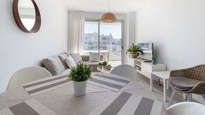 A modern living room with a sofa, a dining table with chairs, a potted plant, and a television on a white console. - Marina Real I - Denia, Costa Blanca (Denia)