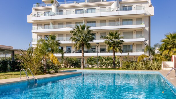 A multi-story hotel with a swimming pool, palm trees, and a clear blue sky. - Marina Real I - Denia, Costa Blanca (Denia)