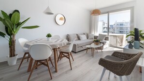 A modern living room with a dining area, a sofa set, and a large window offering a city view. - Marina Real I - Denia, Costa Blanca (Denia)