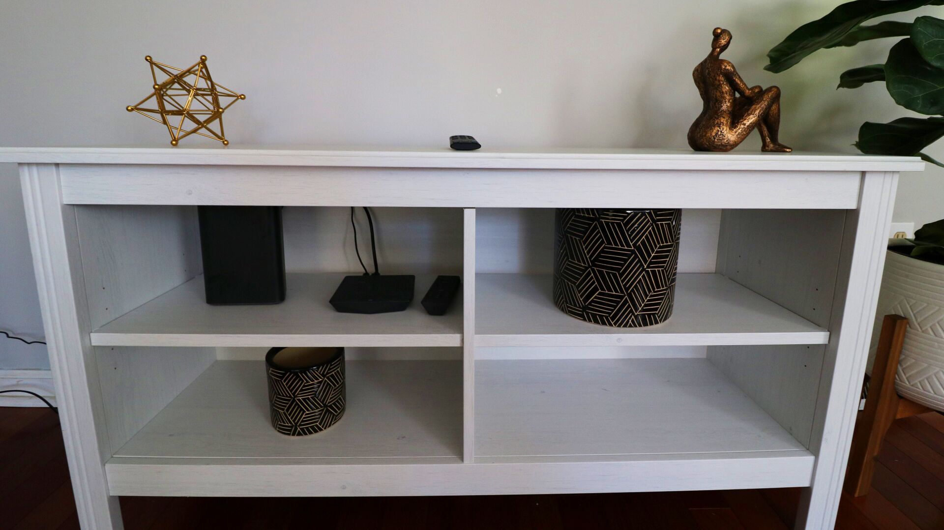 Een witte open kast met drie plateaus, elk versierd met diverse decoratieve objecten.