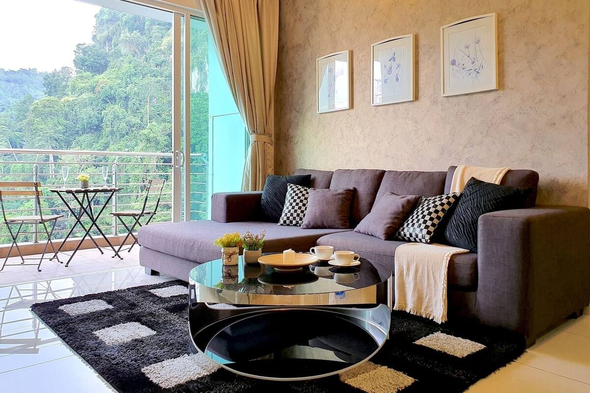 A living room with a sofa, a glass coffee table, and a view of greenery through large windows.