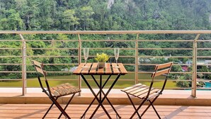 A balcony with a table and chairs, overlooking a lush green valley and a river. - The Haven Residences by BeeStay at Tambun (Ipoh)