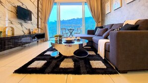 A modern living room with a marble wall, a large window with curtains, a sofa, a coffee table, and a TV mounted on the wall. - The Haven Residences by BeeStay at Tambun (Ipoh)