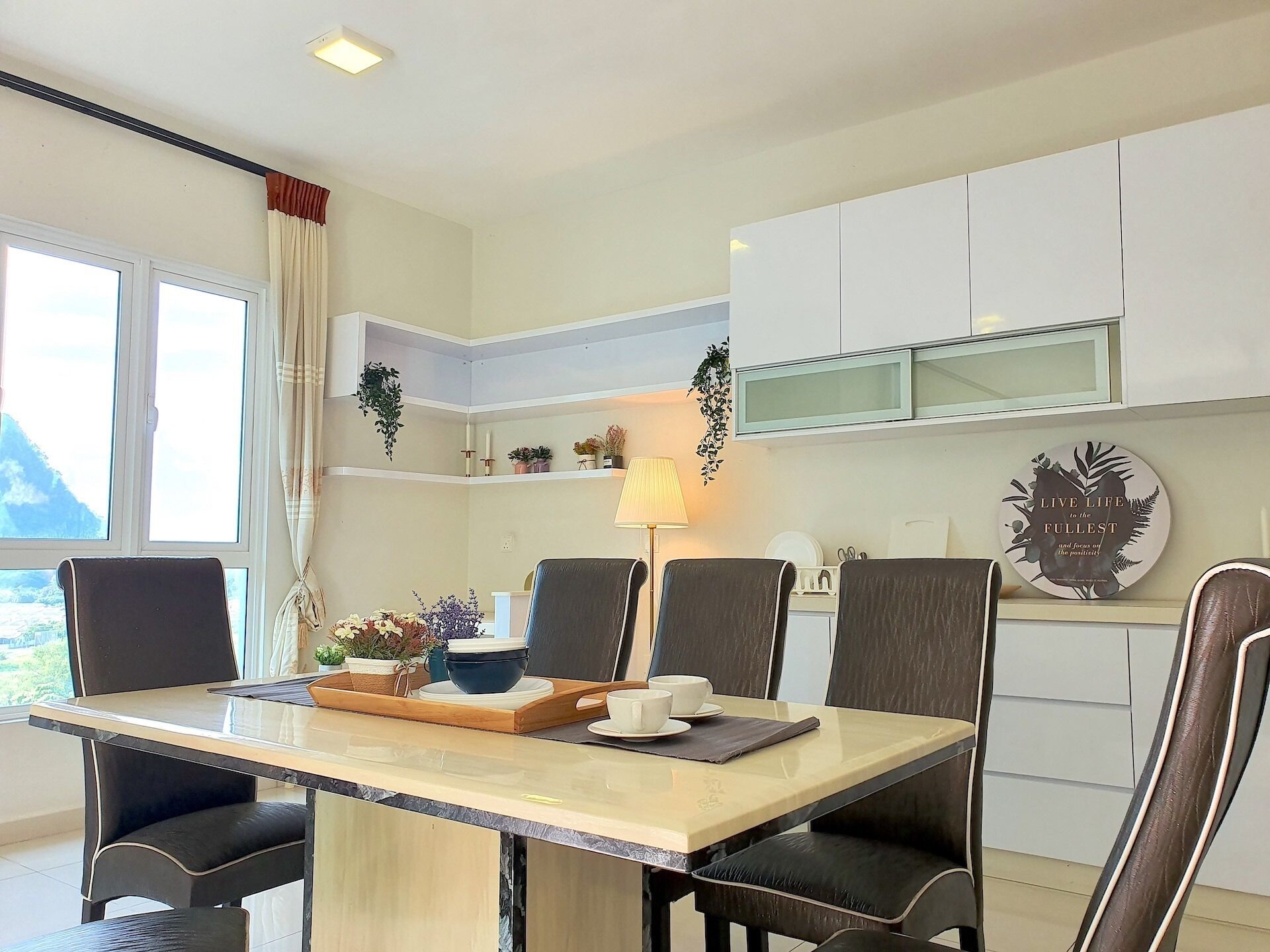 A dining area with a table set for four, chairs, a tray with dishes, and a lamp.