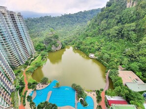 A high-rise hotel with a large swimming pool surrounded by lush greenery and a river.