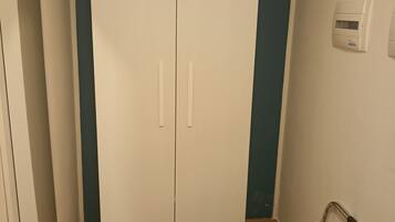 Una habitación con un armario blanco, una silla metálica y un termostato fijado a la pared.