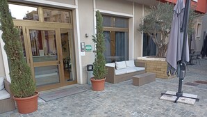 A hotel entrance with a glass door, a seating area with a sofa and cushions, and potted plants. - Palazzo Marignano Hotel (Melegnano)