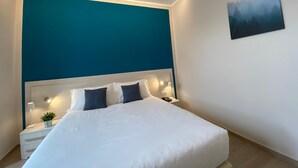 A modern bedroom with a large bed, white bedding, and a teal accent wall. - Palazzo Marignano Hotel (Melegnano)