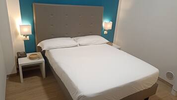 Ein ordentlich bezogenes Bett mit weißen Leinen in einem Zimmer, das durch eine blaue Wand und einen gepolsterten Kopfteil Akzente setzt.