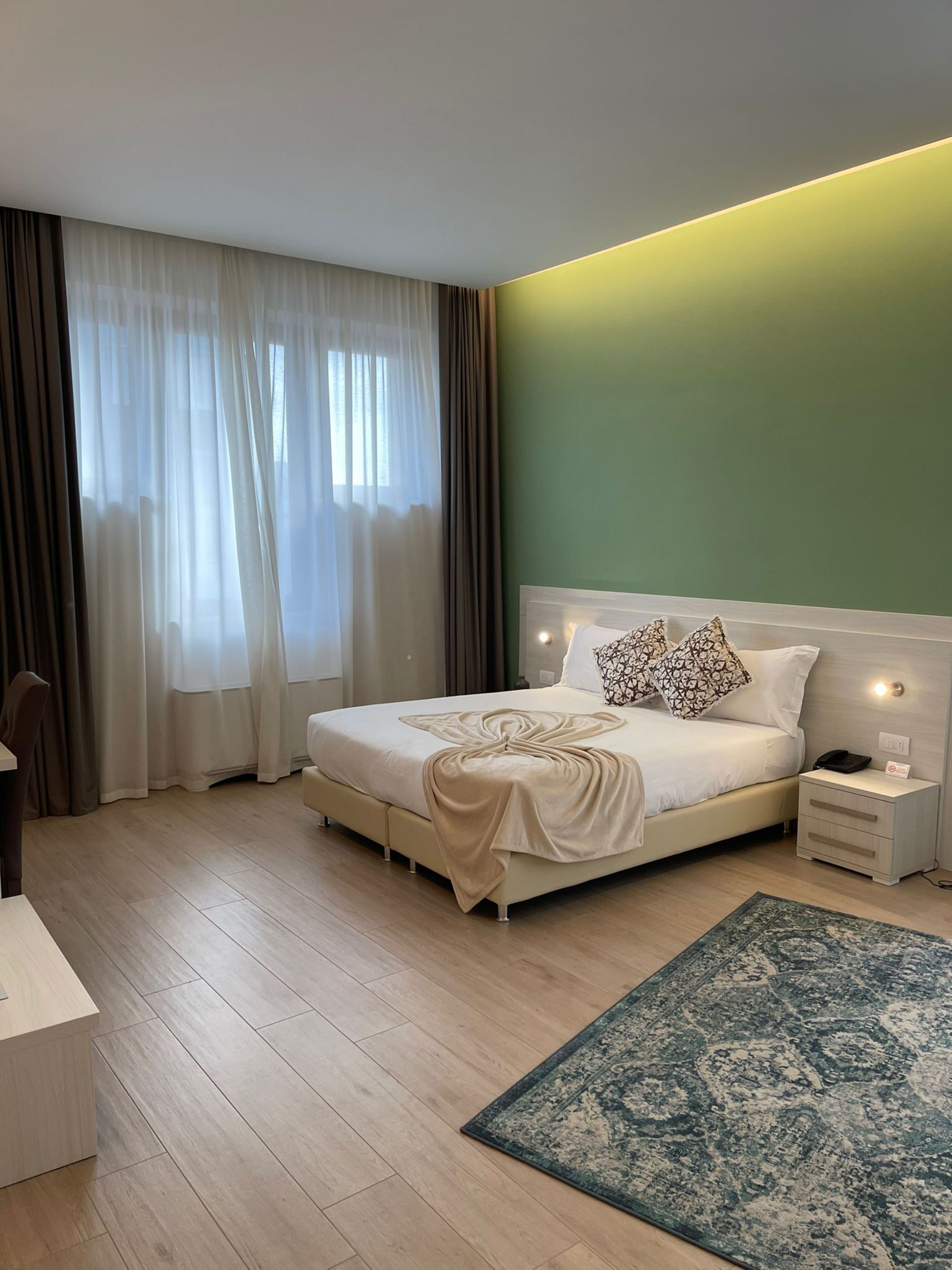 Un dormitorio ordenado con cama, mesitas de noche, escritorio y una alfombra estampada.