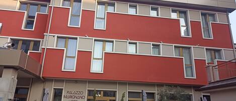 A multi-story hotel with a red facade, large windows, and a sign reading "PALAZZO MARIGNANO HOTEL".