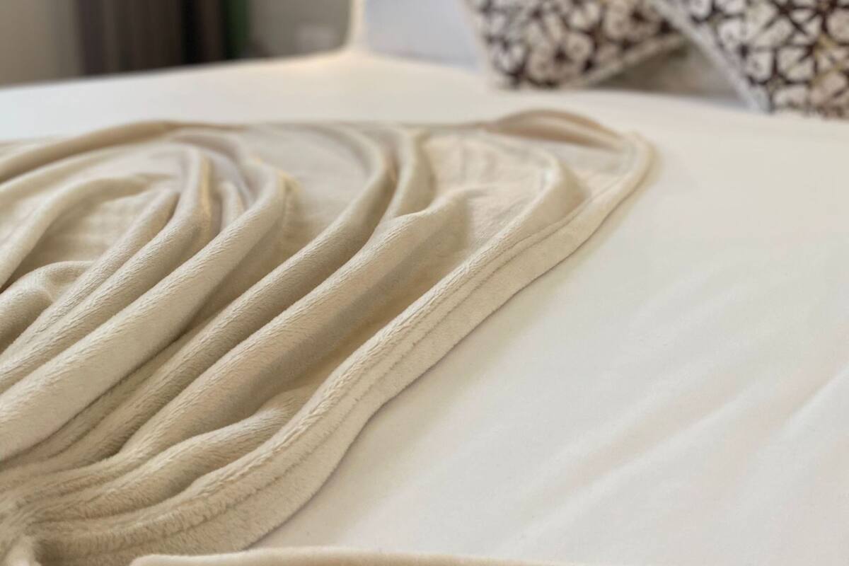 Ein ordentlich bezogenes Bett mit weißer Laken und beiger Decke, zwei gemusterte Kissen und eine grüne Wand im Hintergrund.