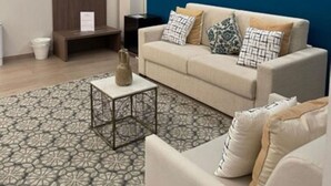 A modern living room with a blue accent wall, a beige sofa with patterned cushions, a small coffee table, and a decorative vase. - Palazzo Marignano Hotel (Melegnano)