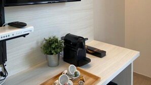 A modern room with a flat-screen TV mounted on the wall, a coffee maker, a tray with cups and a plant on the counter. - Palazzo Marignano Hotel (Melegnano)