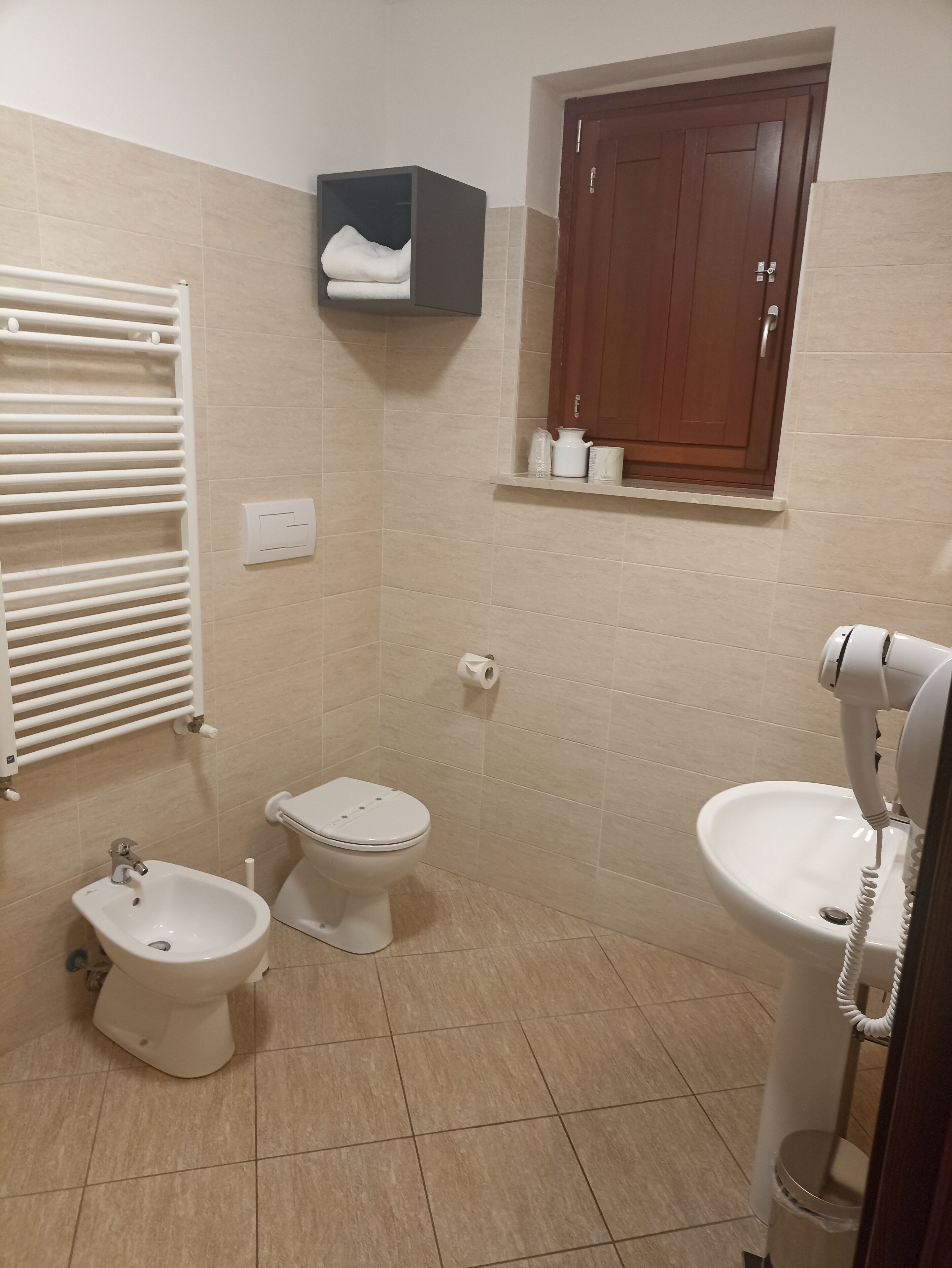 A bathroom with a bidet, toilet, sink, towel rack, and a cabinet with toiletries.