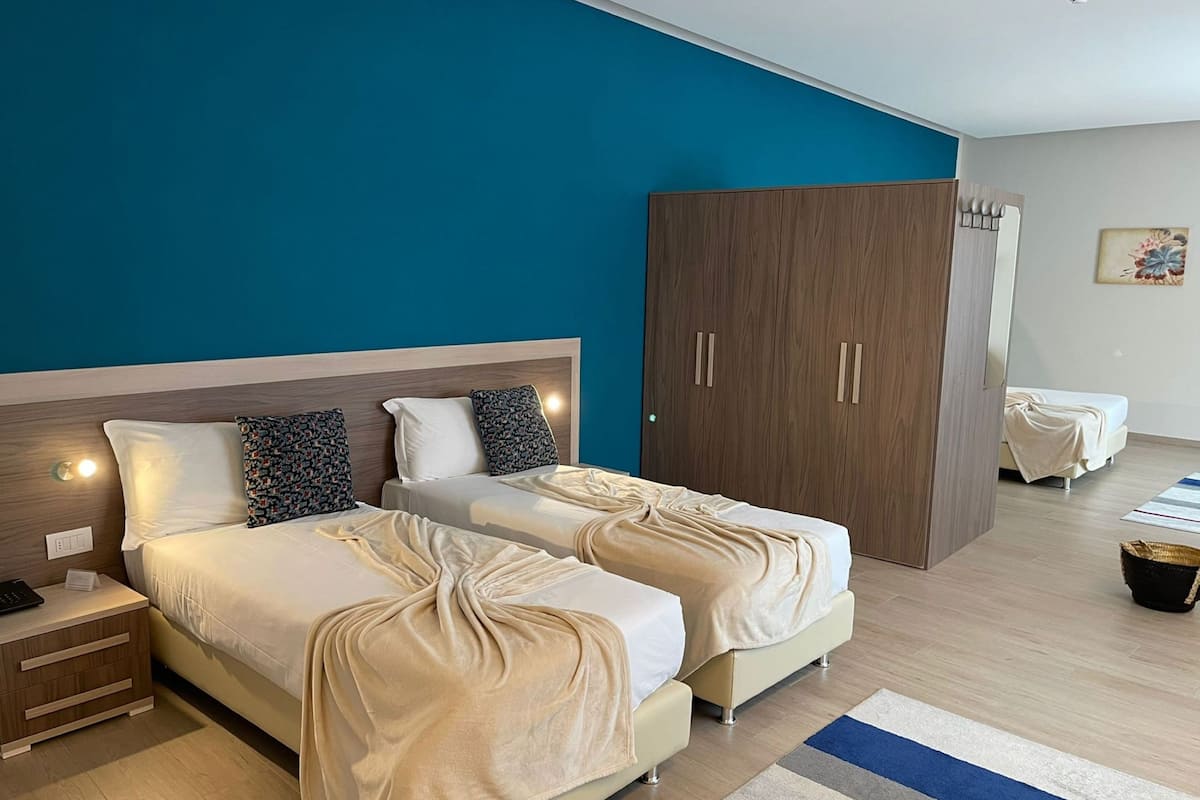 Ein Hotelzimmer mit zwei Betten, einem Kleiderschrank, einem Nachttisch und einem Beistelltisch.