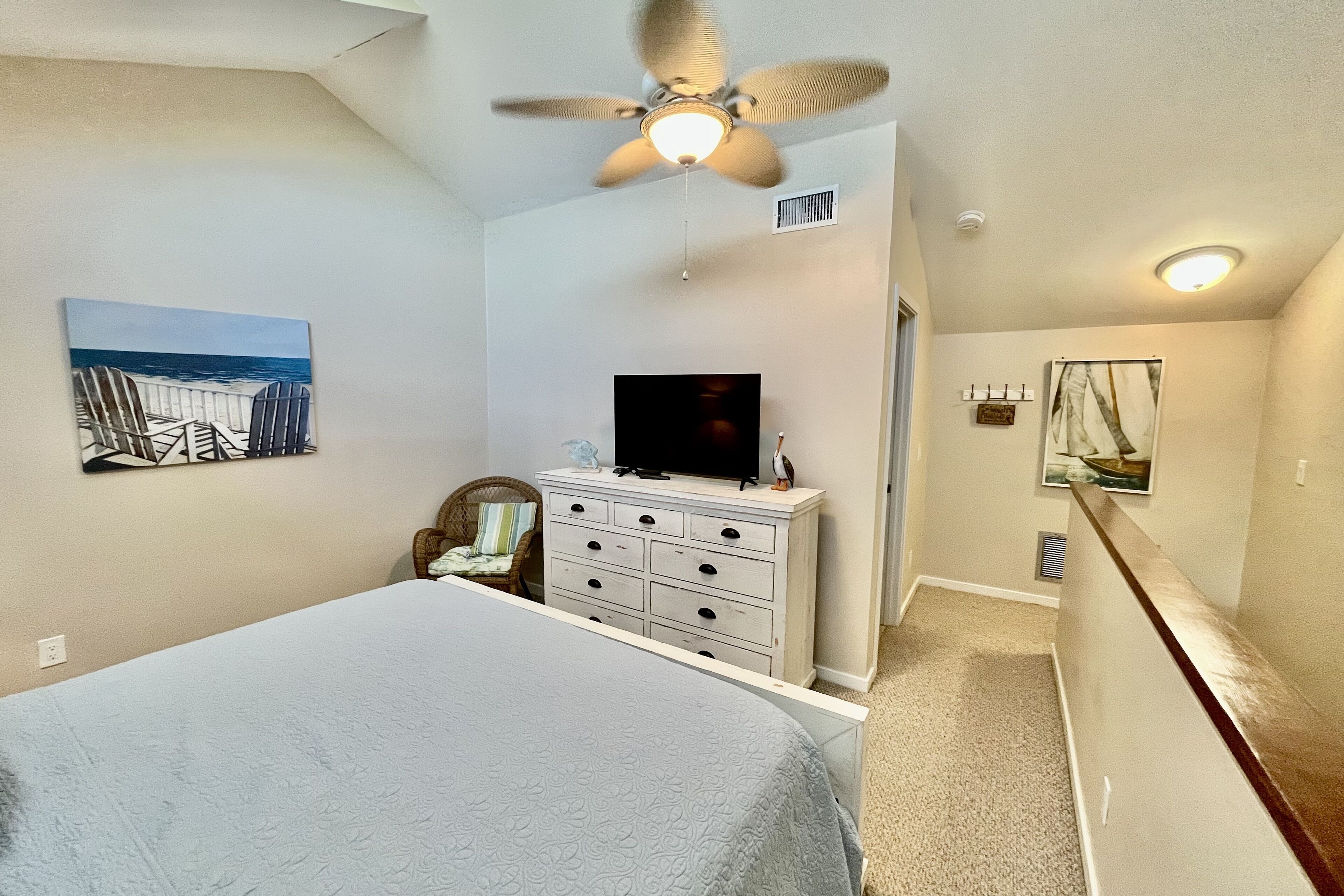 A bedroom with a bed, a dresser, a television, and a ceiling fan.
