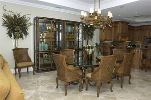 A dining area with a glass-top table surrounded by six chairs, a chandelier, and a large glass cabinet with kitchenware.