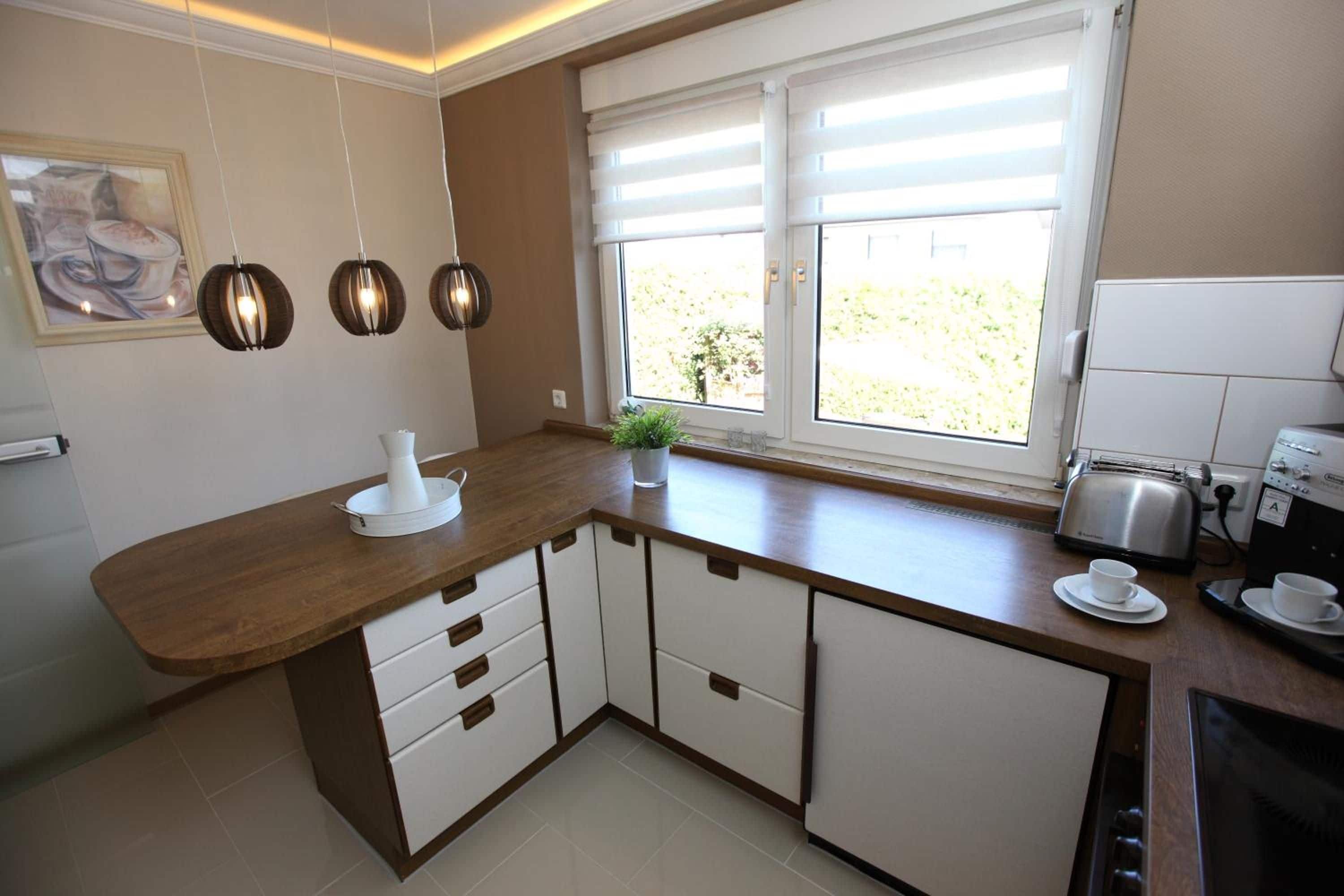 A kitchen with a wooden countertop, white cabinets, a coffee machine, and a window with blinds.