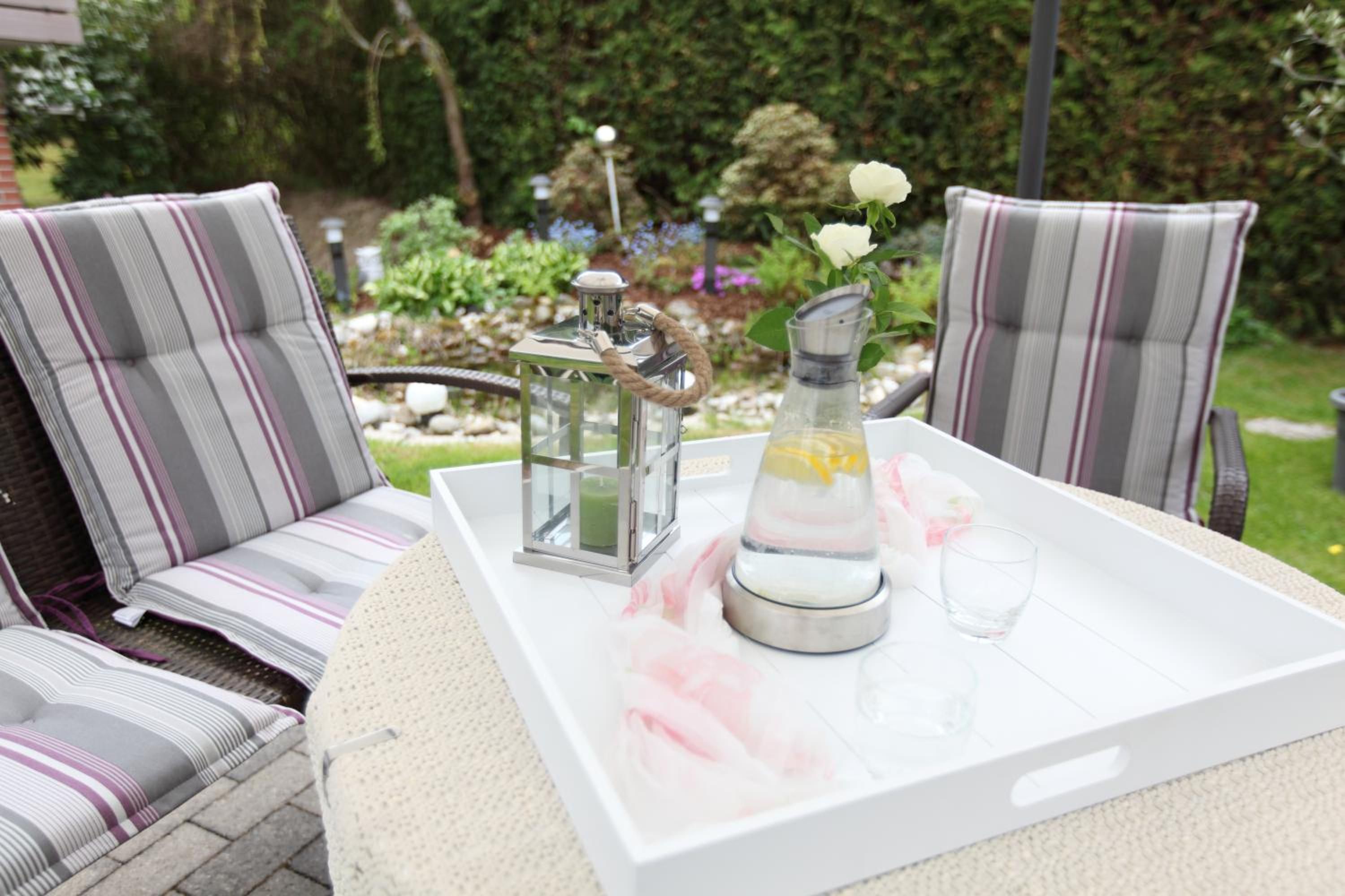 A patio with two striped chairs, a white table with a glass pitcher, a candle, and a glass.