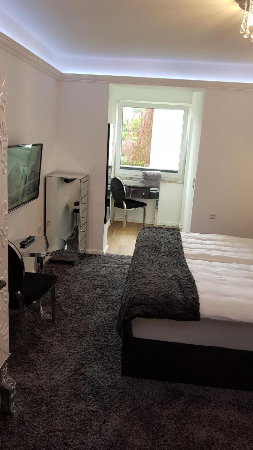 A bedroom with a bed, a desk, a chair, a television, and a window.