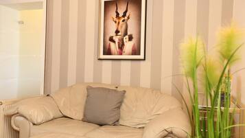 A room with a striped wall, a framed picture of an animal, a beige sofa with a pillow, and a plant.