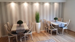 A dining area with two tables, chairs, a potted plant, and a striped wall.