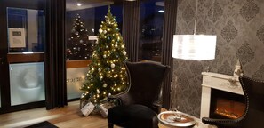 A room with a Christmas tree, a fireplace, and a chair.