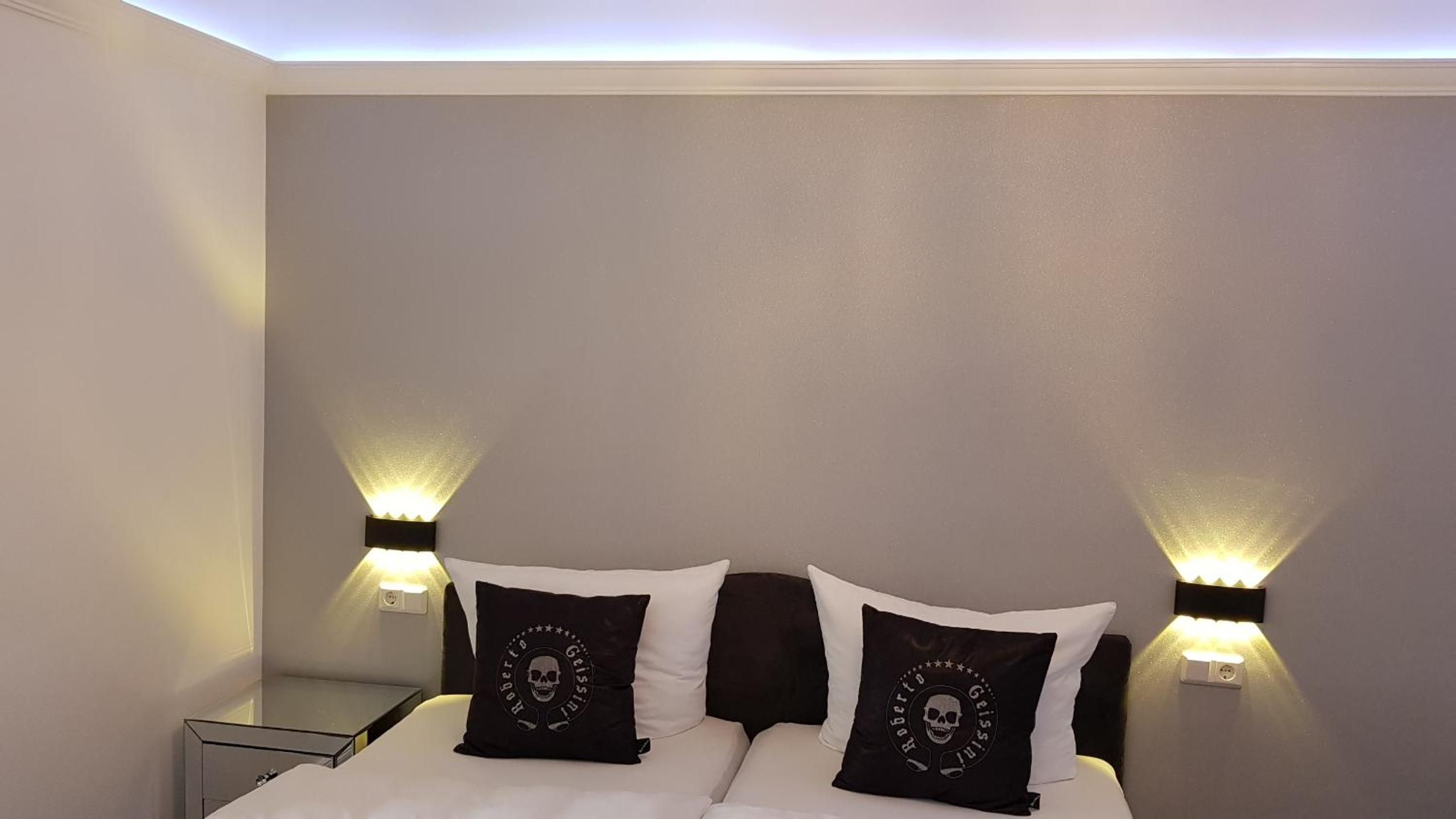 A hotel room with a bed, two bedside lamps, and two pillows with skull designs.