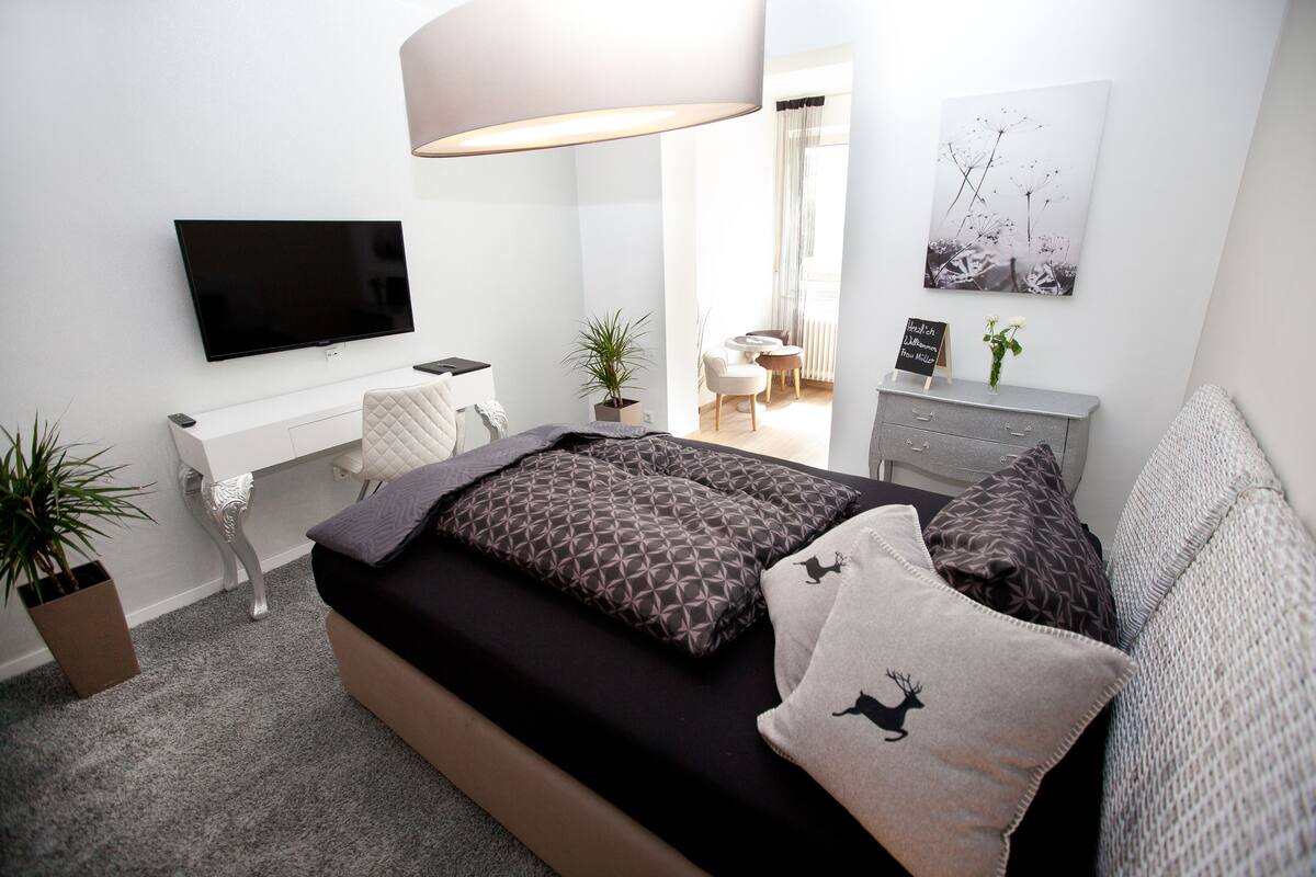 Een moderne slaapkamer met een bed, een bureau, een televisie en een zithoekje.
