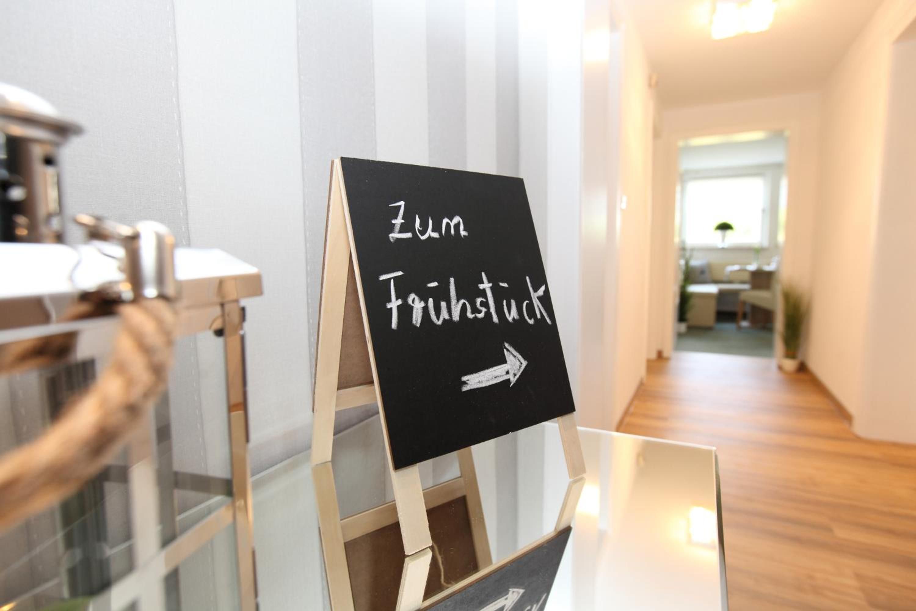 Ein Schild in einer Diele mit dem Schriftzug 'Zum Frühstück' und einem nach rechts zeigenden Pfeil.