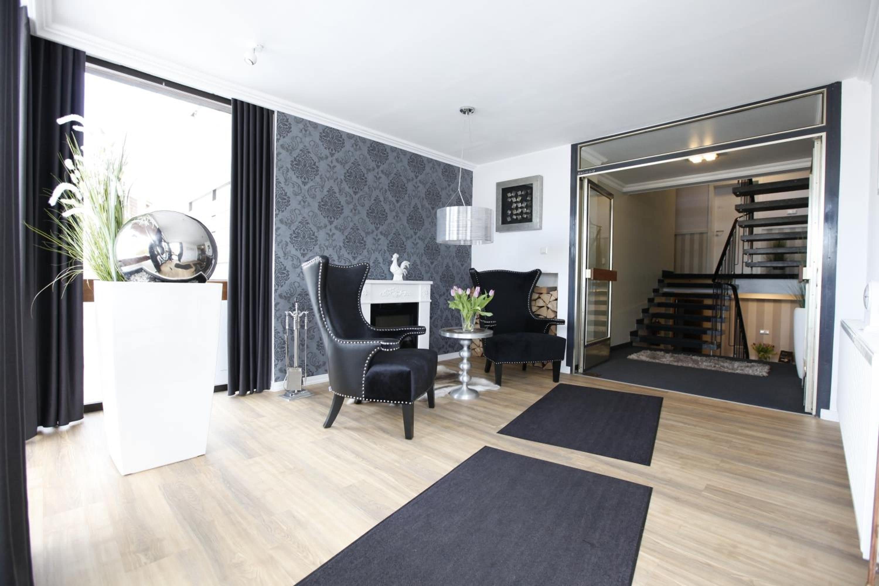 Een moderne woonkamer met een open haard, twee zwarte fauteuils, een ronde tafel en een trap naar een hoger gelegen verdieping.