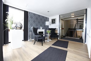A modern living room with a fireplace, two black armchairs, a round table, and a staircase leading to an upper level.