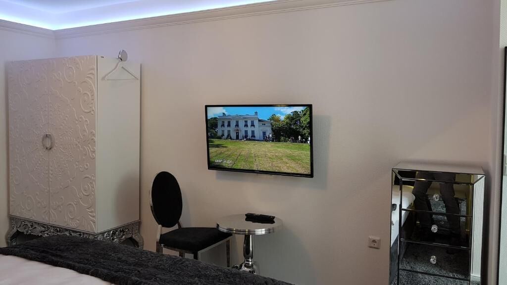 A hotel room with a bed, a chair, a small table, a TV mounted on the wall, and a mirror.