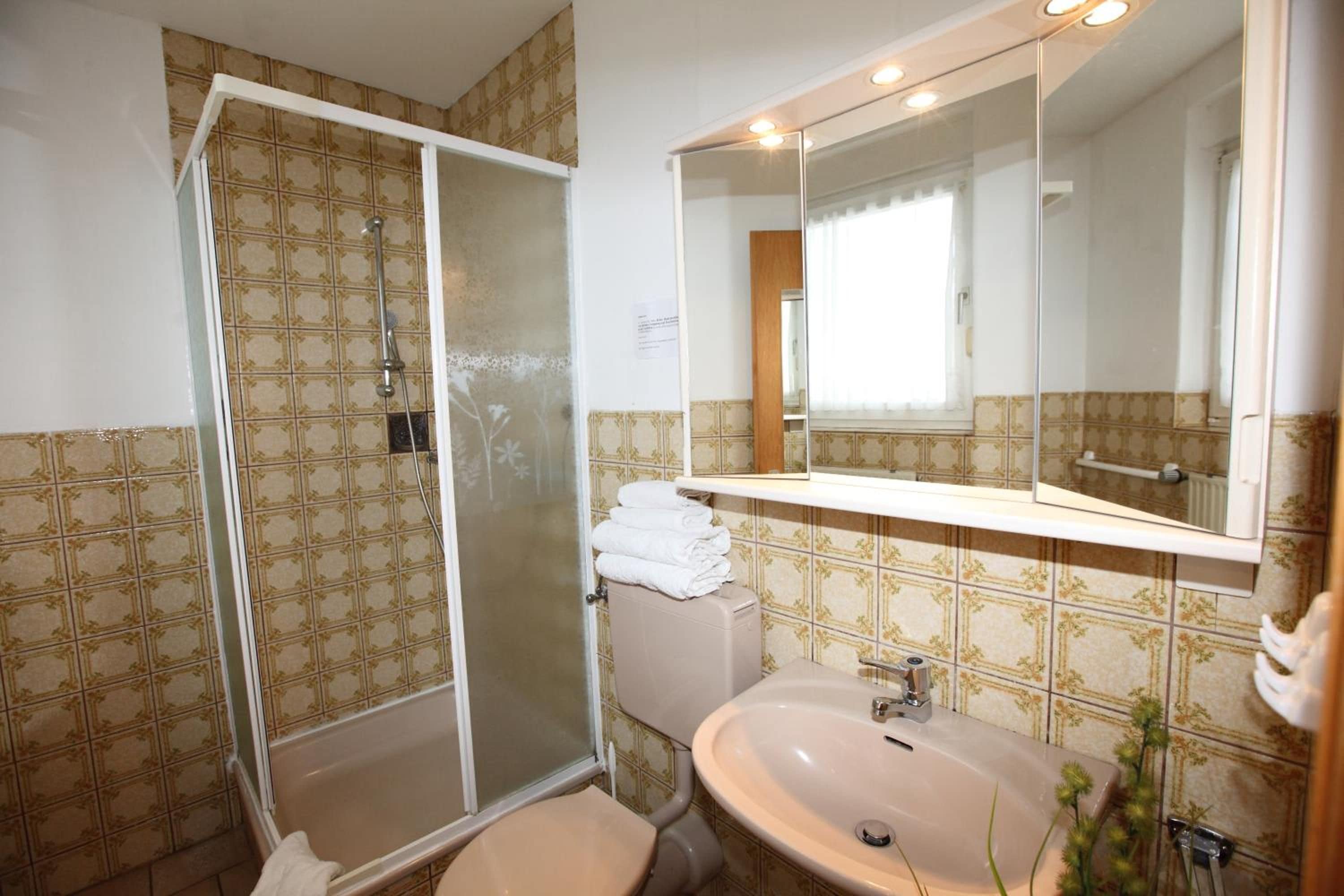 Un baño con ducha, inodoro, lavamanos y un espejo grande.
