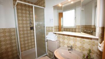 A bathroom with a shower, toilet, sink, and a large mirror.